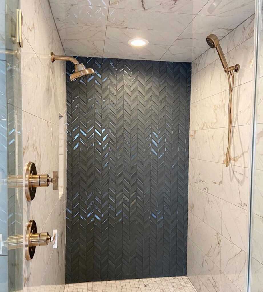 Dark grey herringbone patterned tiles forming an accent wall inside a marble shower stall.