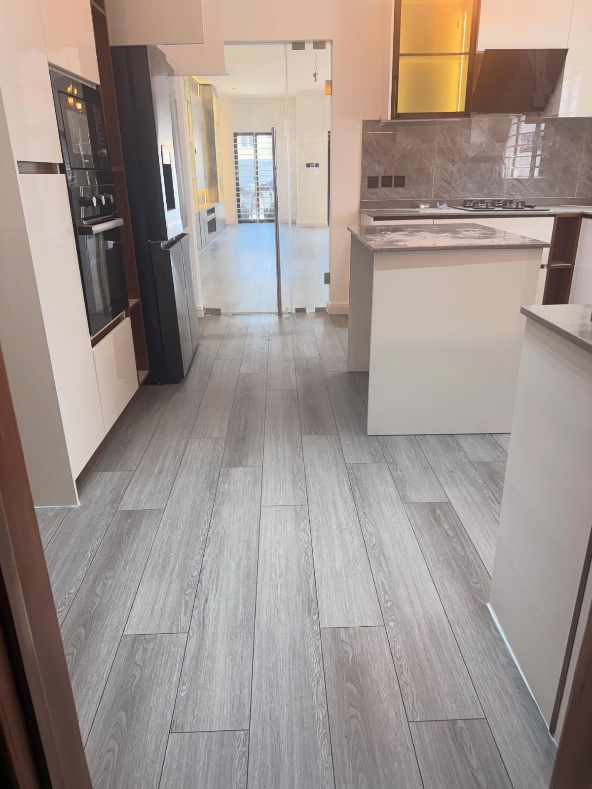 Grey wood-textured floor planks in a modern white kitchen with dark appliances.