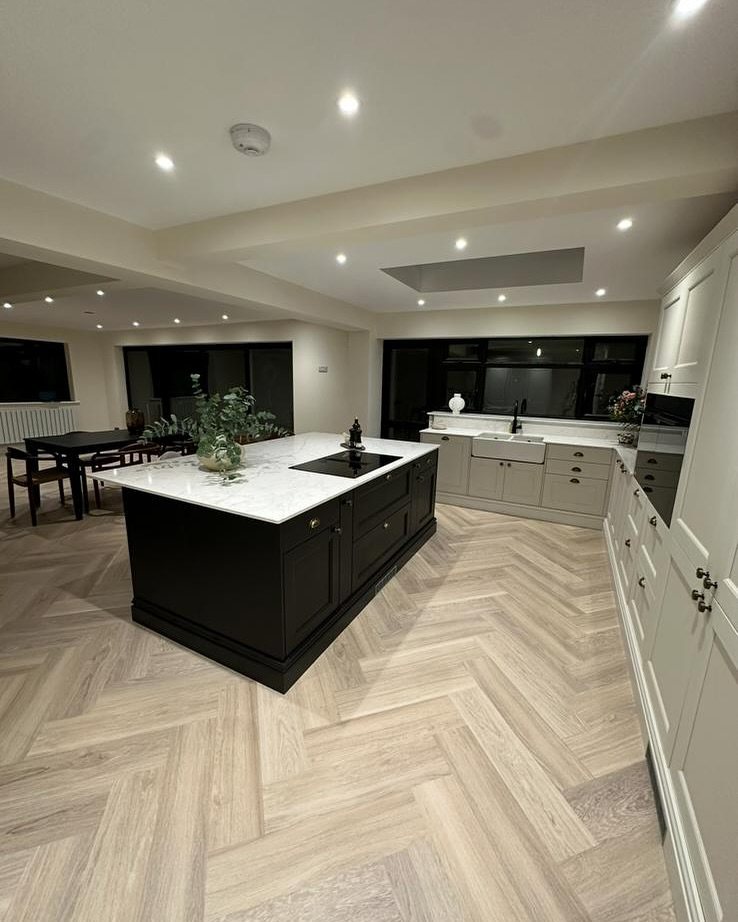 Light wood herringbone flooring in a modern kitchen with a black island and grey cabinets.