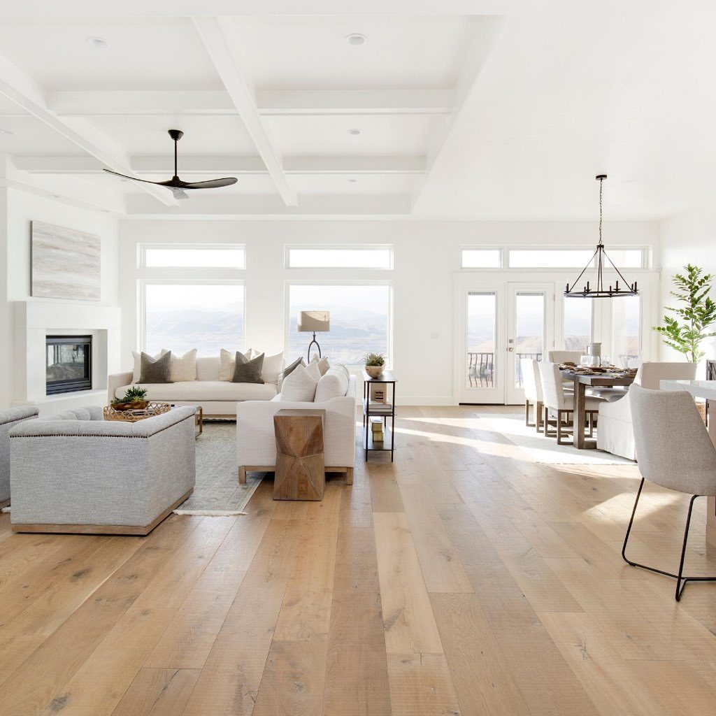 Light wood flooring in a bright, modern open-concept living and dining room with white walls.