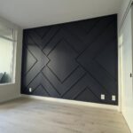Geometric dark grey accent wall with raised wooden slats in a modern room with light flooring.