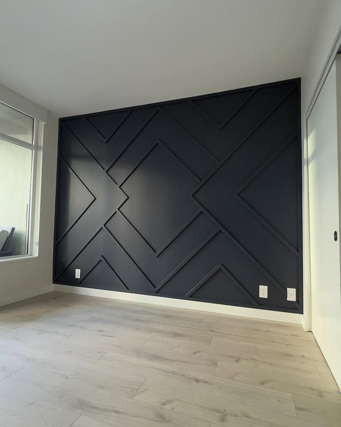 Geometric dark grey accent wall with raised wooden slats in a modern room with light flooring.