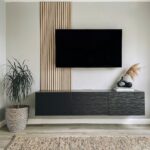 Vertical light wood slats mounted on a grey wall behind a black television and media console.