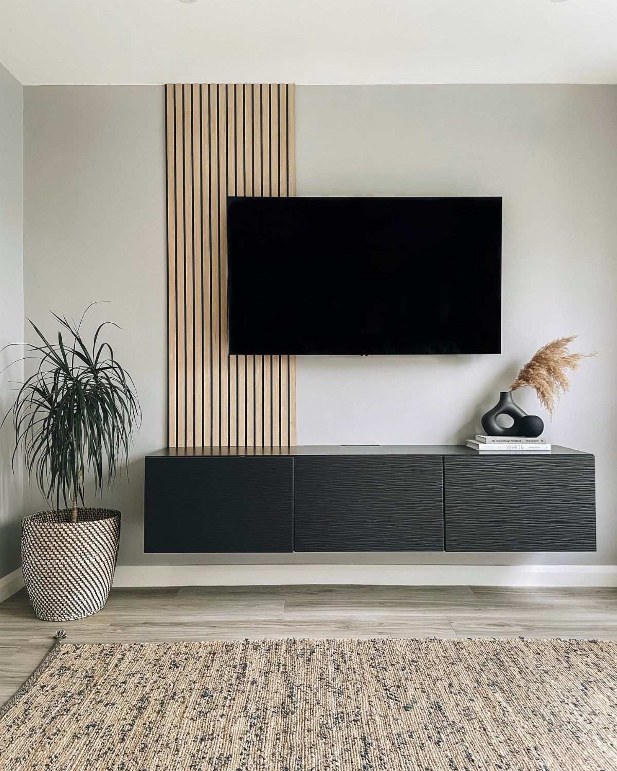 Vertical light wood slats mounted on a grey wall behind a black television and media console.