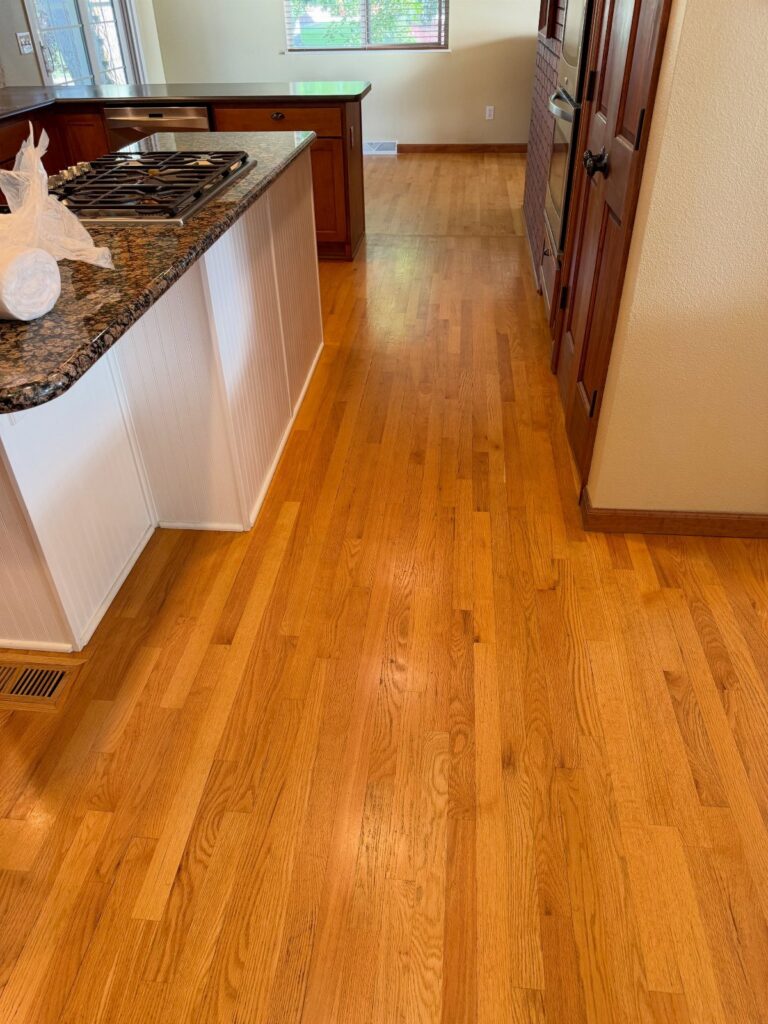 Light brown wooden plank flooring in a kitchen with granite countertops and dark wood cabinets.